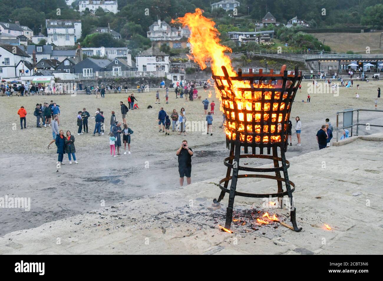 Lyme Regis, Dorset, Großbritannien. August 2020. Der 75. Jahrestag des VJ Day markiert das Ende des Krieges mit Japan auf der Cobb Harbour Wall bei Lyme Regis in Dorset gedenkt. Die Zuschauer beobachten die Flammen des Leuchtfeuers, wie es brennt. Bild: Graham Hunt/Alamy Live News Stockfoto