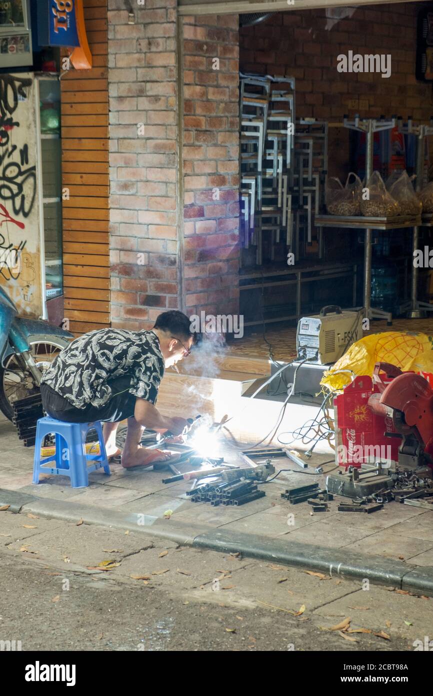 Hanoi, Vietnam - April 21 2019: Porträt eines sitzenden Mannes, der auf der Straße Stahl raucht und schweißt. Stockfoto