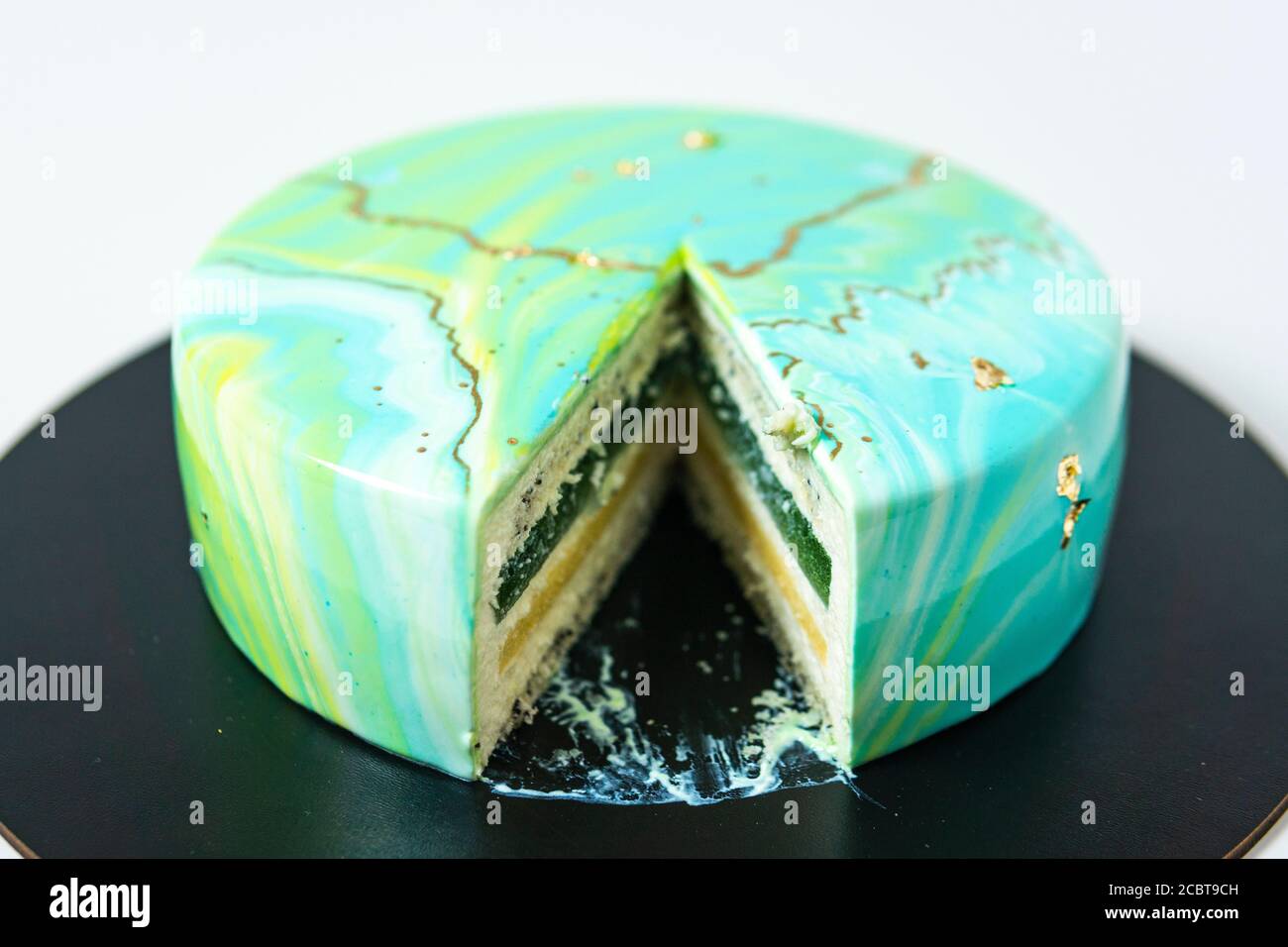 Nahaufnahme von Mousse Kuchen bedeckt blauen und grünen Spiegel Glasur. Französisches Dessert. Gefrorene Spiegel Sahnehäubchen auf dem Kuchen. Backen und Süßwaren Konzept. Weiß Stockfoto