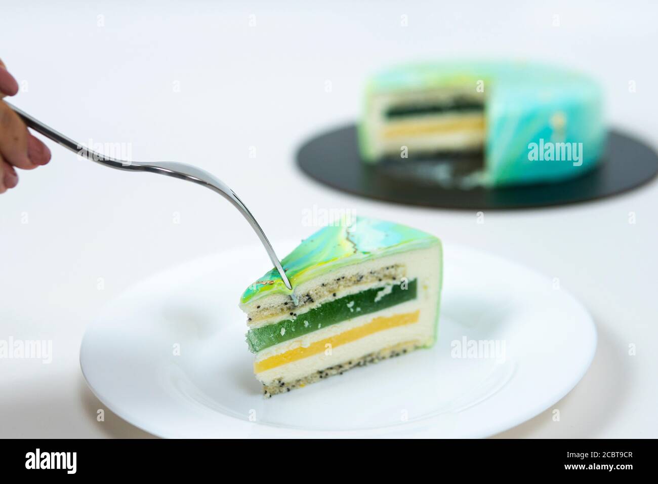 Nahaufnahme Essen Scheibe Mousse Kuchen bedeckt blau und grün Spiegelglasur. Französisches Dessert. Gefrorener Spiegel Sahnehäubchen auf dem Kuchen. Backen und Süßwaren Co Stockfoto