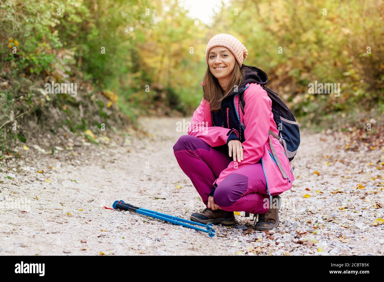 Hiker Mädchen hocken auf einem breiten Weg in den Bergen. Rucksacktourist mit rosa Jacke in einem Wald. Gesunder Fitness-Lebensstil im Freien. Stockfoto