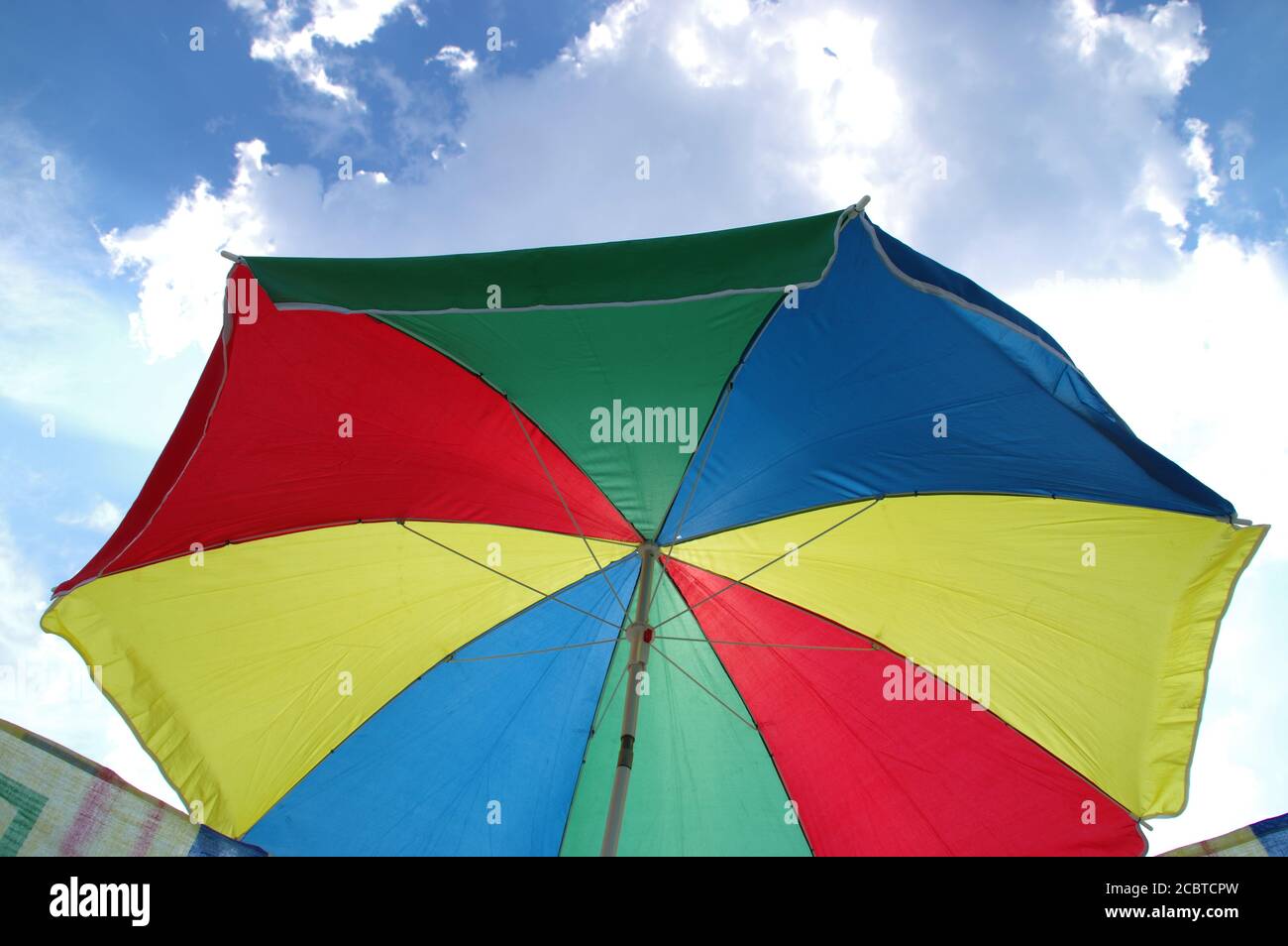 Sonnenschirm am Strand auf dem Hintergrund von Wolken und Himmel. Urlaub am Meer. Farbenfroher Sonnenschirm. Stockfoto