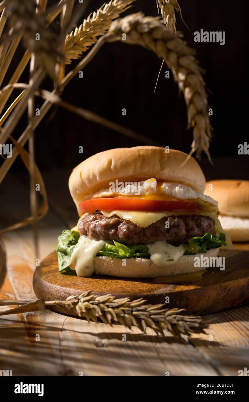 Street Food, Fast-Pub-Essen. Hausgemachte saftige Burger mit Rind, Käsestomate, Salat und Eierzwiebeln auf Holztisch. Scharfes Licht für die Sommerernte moo Stockfoto