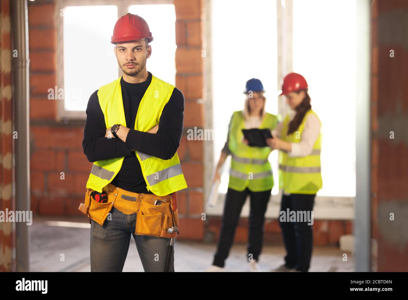 Männlicher Arbeiter auf einer Wohnbaustelle mit seinem Team Von Ingenieuren, die im Hintergrund arbeiten Stockfoto