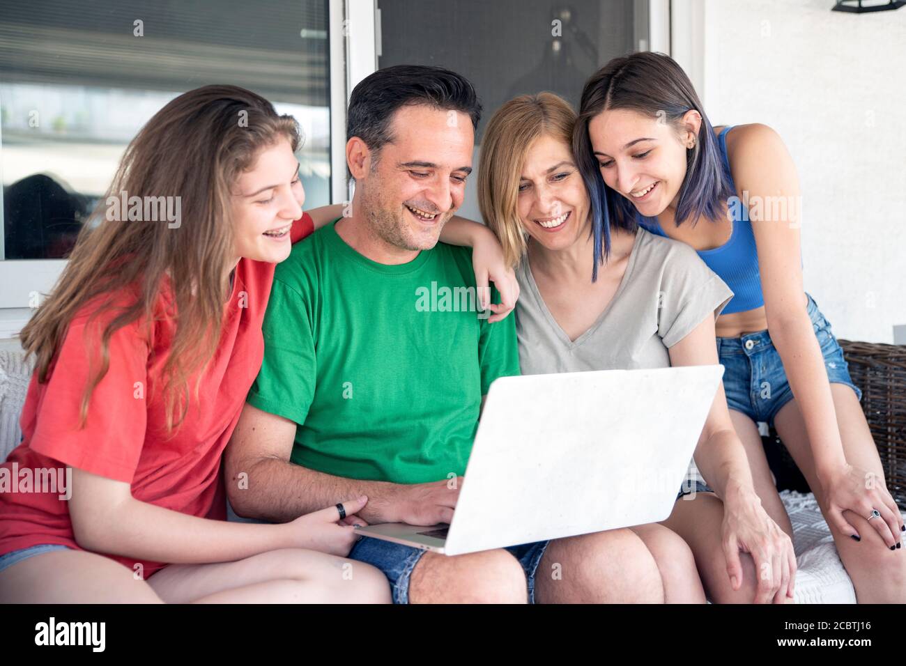 Glückliche Familie Mit Zwei Töchtern Mit Laptop Zusammen. Sitzen auf einem Sofa auf dem Balkon Stockfoto