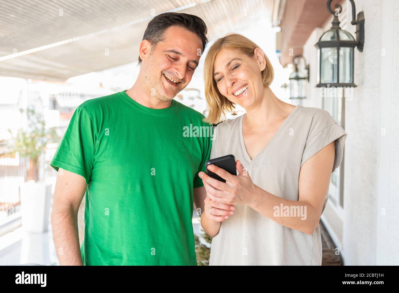 Ein Paar, eine Frau und ein Mann mittleren Alters benutzen ein Smartphone auf dem Balkon. Tageslicht Stockfoto