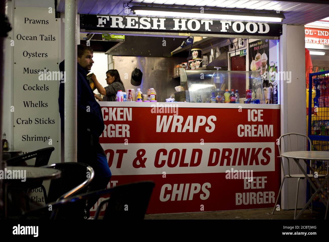 Mann, der vor einem Straßenhändler wartet, nimmt es mit. Düstere Szene, spät abends essen, frisches warmes Essen, Blackpool Promenade, schnelles Essen, Street Photography, Stockfoto