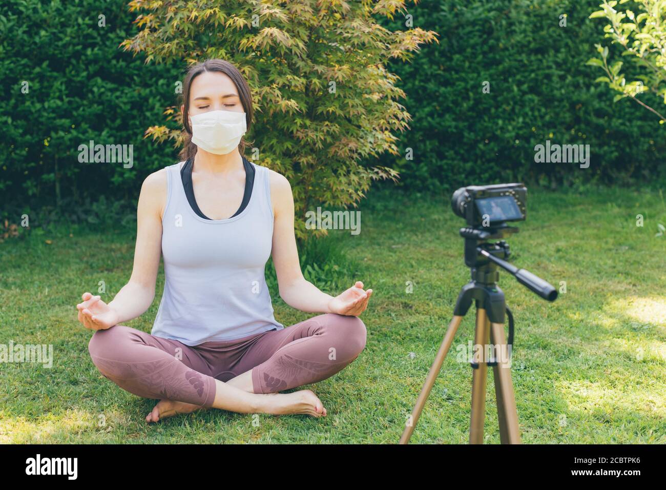 Junge Bloggerin macht Video über "wie Yoga zu machen Mit medizinischer Maske während oder nach Quarantäne' - vlogging about Leben nach dem COVID-19 Konzept Stockfoto