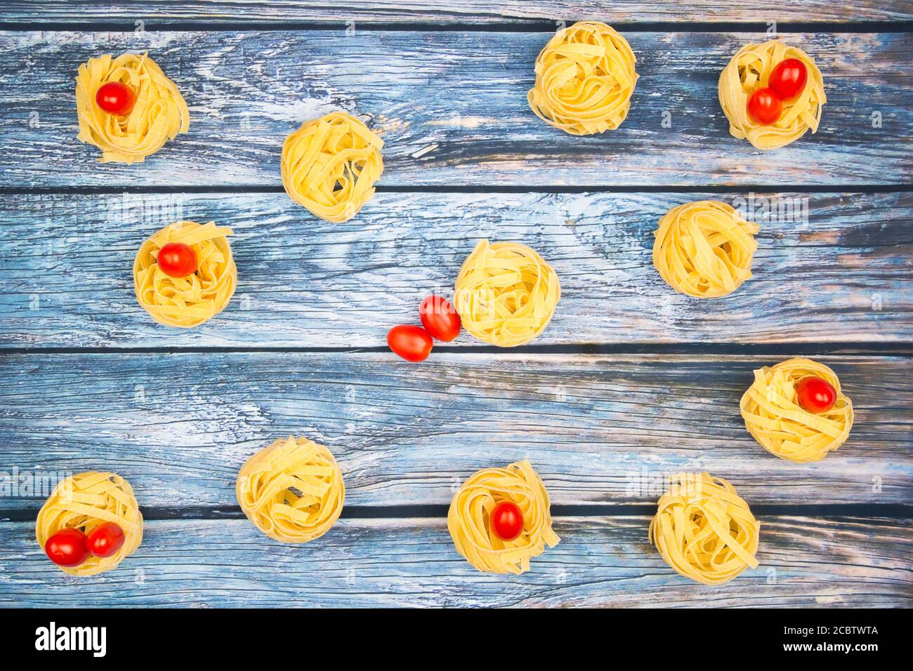 Nester von Tagliatelle-Nudeln mit eiförmigen Mini-roma-Tomaten auf einem verwitterten bläulichen Tisch. Stockfoto