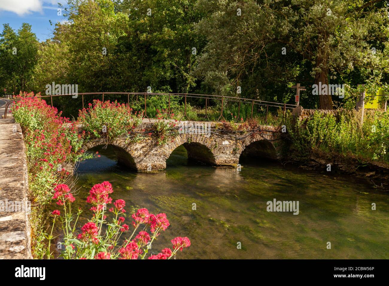 Die alte Steinbrücke am Fluss Colne blüht im Vordergrund bei Bilbury, Cotswold, England Stockfoto