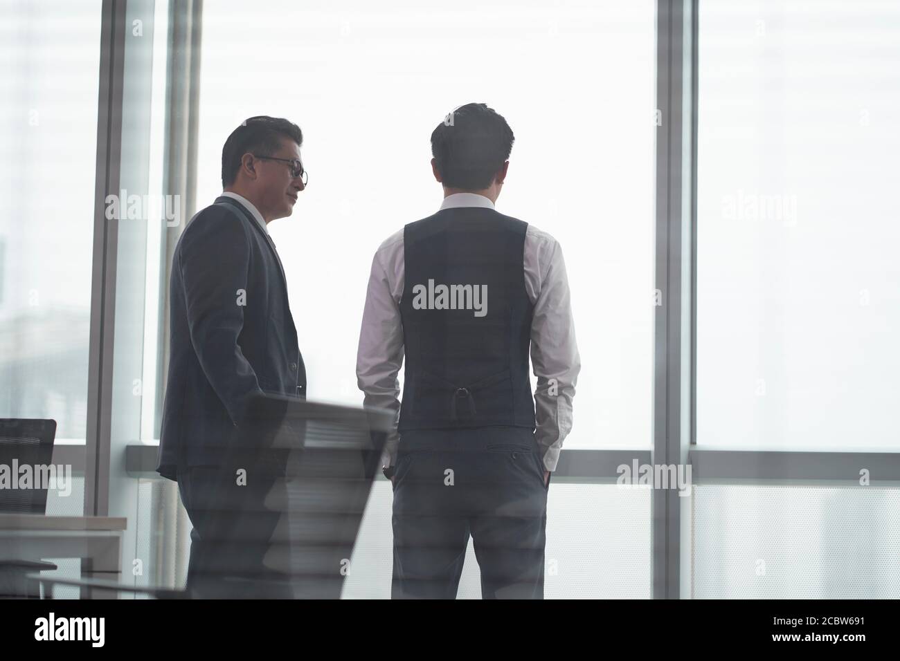 Rückansicht von zwei asiatischen Geschäftsleuten, die davor standen Des Bürofensters mit einer Diskussion Stockfoto
