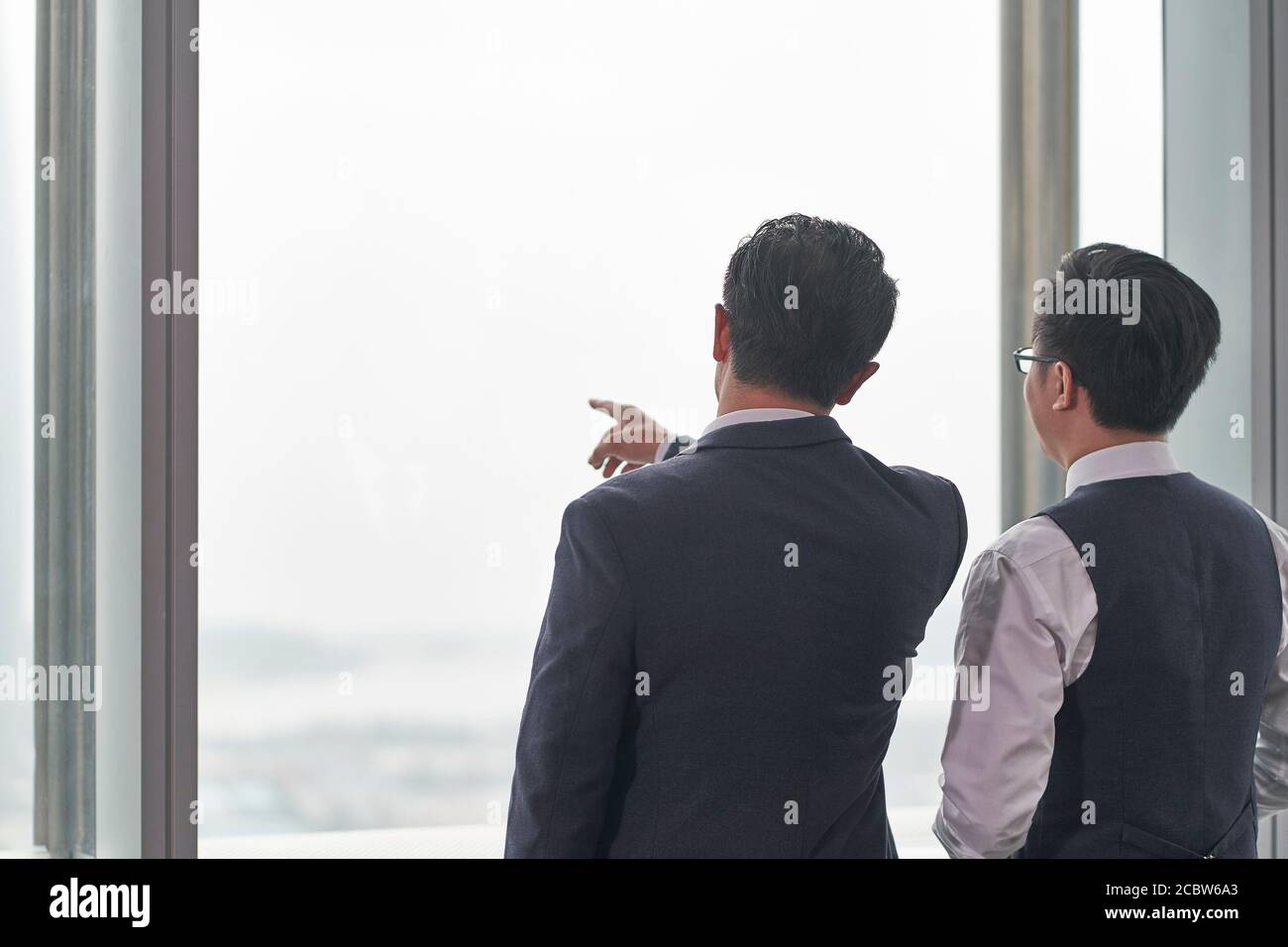 Rückansicht von zwei asiatischen Geschäftsleuten, die davor standen Des Bürofensters mit einer Diskussion Stockfoto