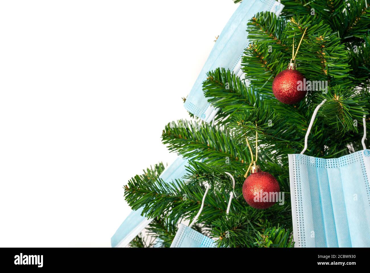 Horizontales Farbbild mit einer Vorderansicht eines Weihnachtsbaums, der mit roten Kugeln und blauen Coronavirus-Masken geschmückt ist. Covid und glückliches neues Jahr Konzept. Stockfoto