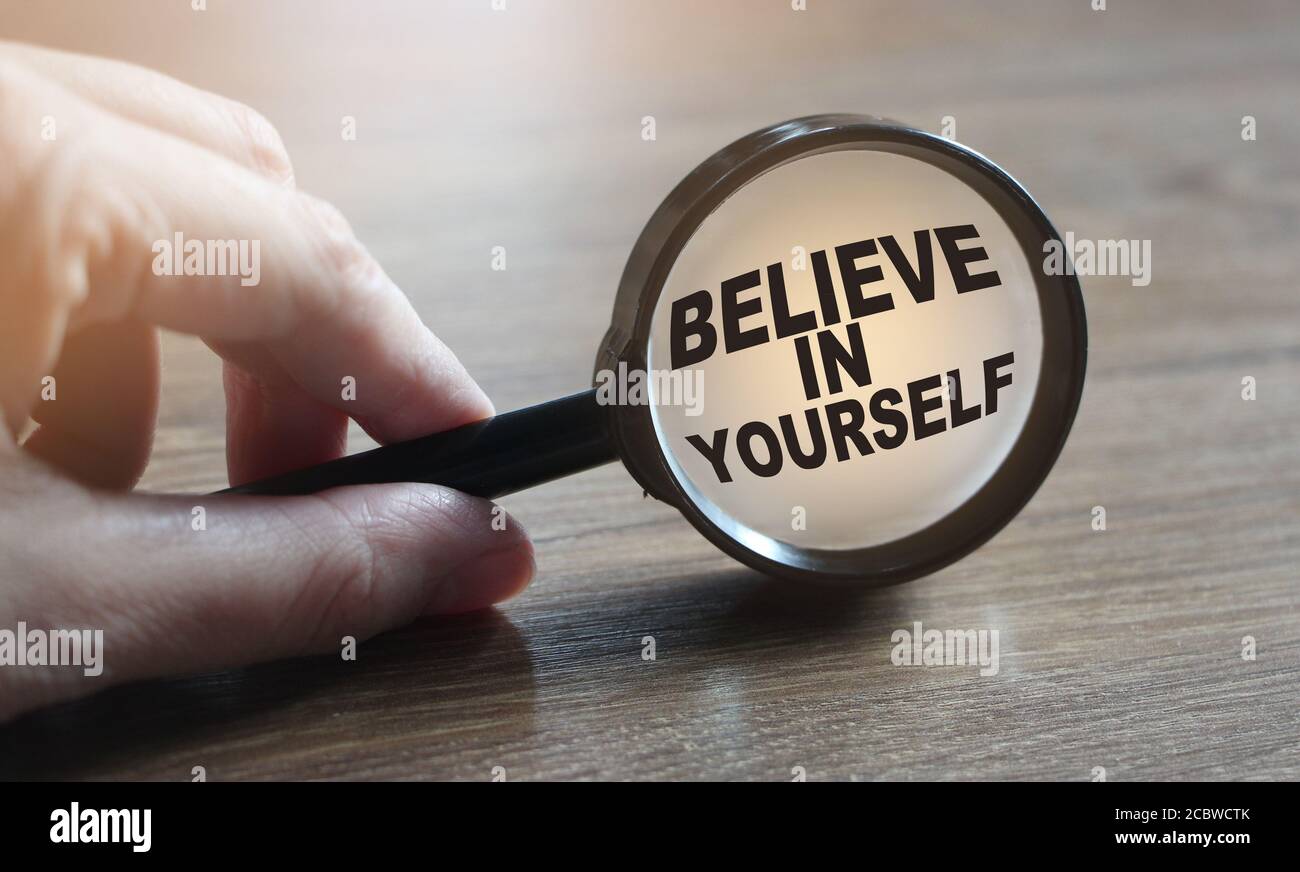 Vergrößerungsglas und Phrase glauben Sie an sich selbst auf Holztisch. Motivationskonzept Stockfoto