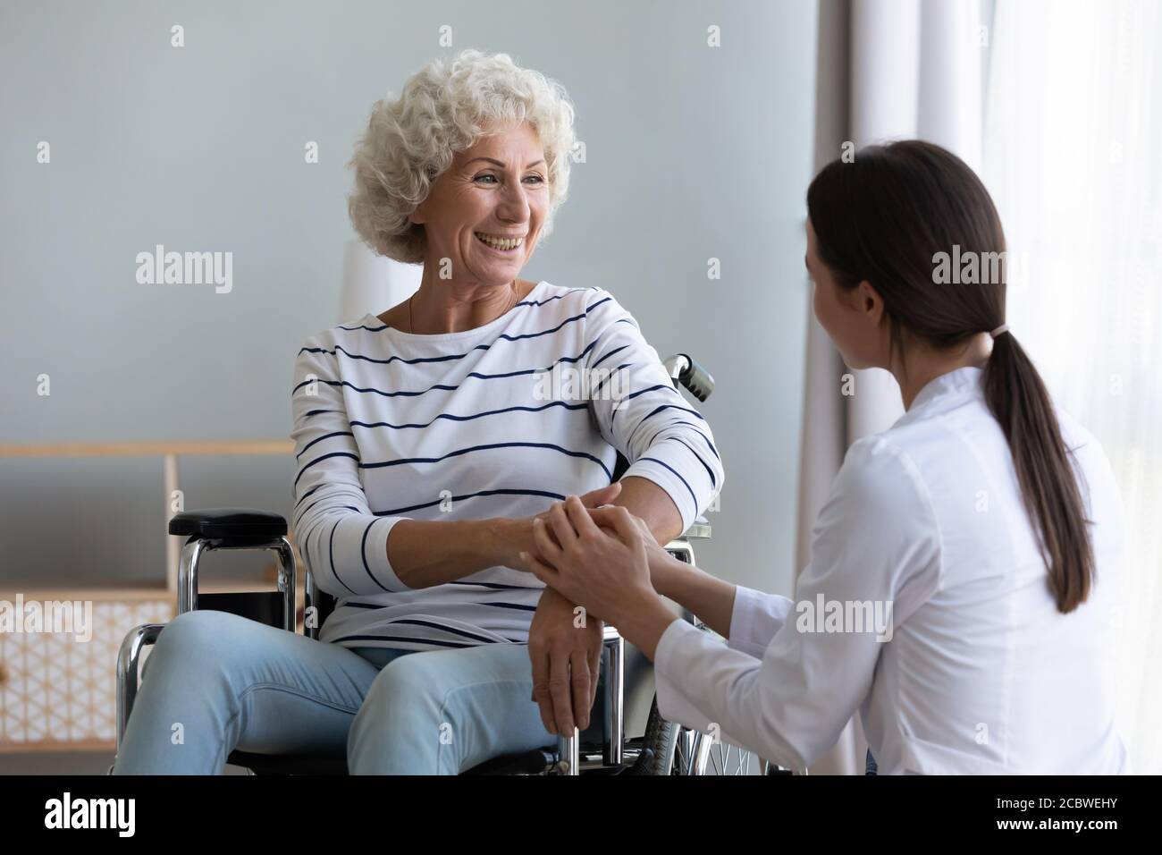 Junge medizinische Mitarbeiterin, die dem glücklichen alten Patienten psychologische Hilfe gibt. Stockfoto