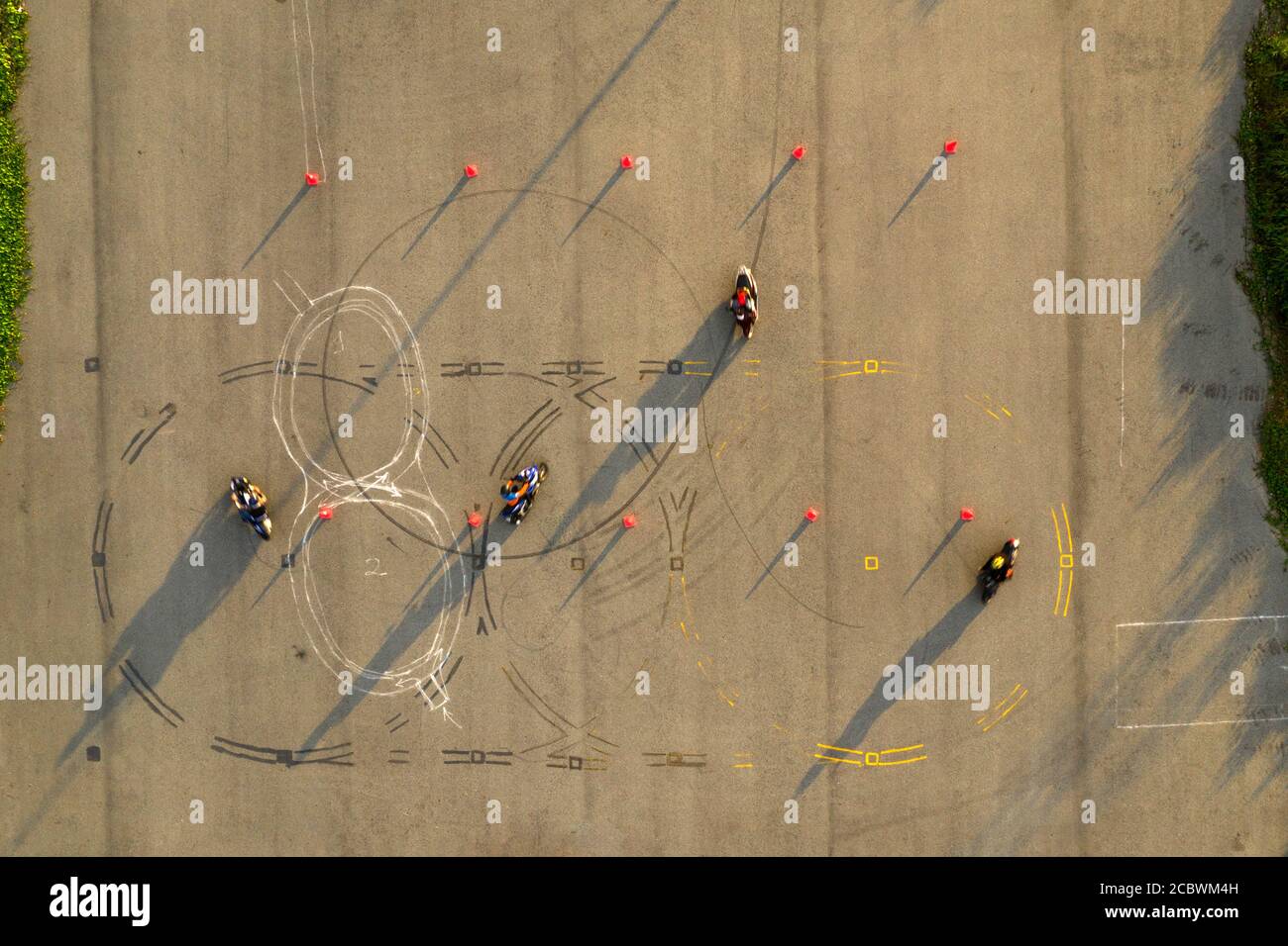 Von oben nach unten breite Luftaufnahme von vier Fahrern, die Spaß auf einem fortgeschrittenen Motorrad-Slalom-Kurs zwischen orangen Kegeln mit langen Schatten haben, bemalt Stockfoto
