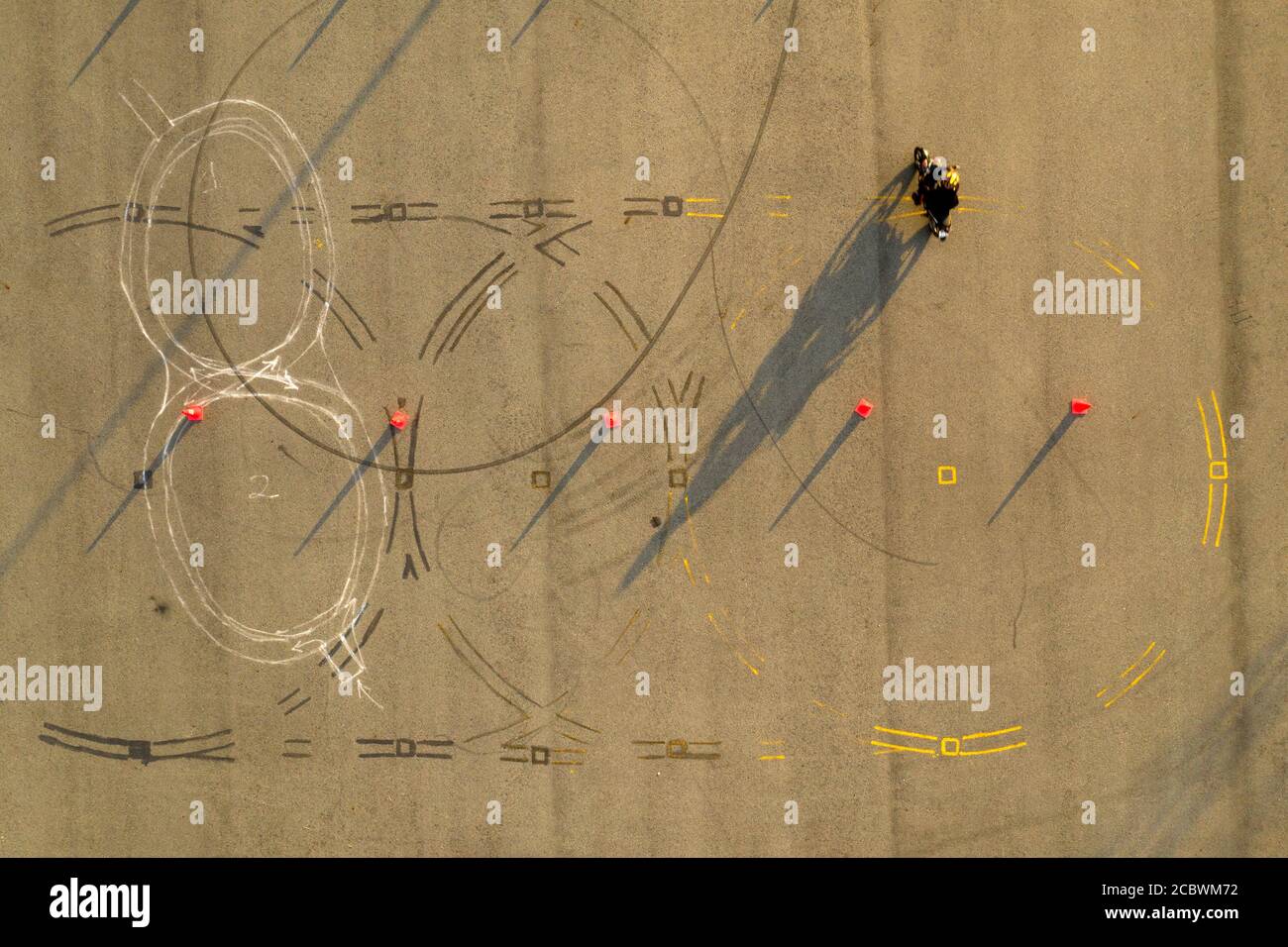 Von oben nach unten breite Luftaufnahme von vier Fahrern, die Spaß auf einem fortgeschrittenen Motorrad-Slalom-Kurs zwischen orangen Kegeln mit langen Schatten haben, bemalt Stockfoto
