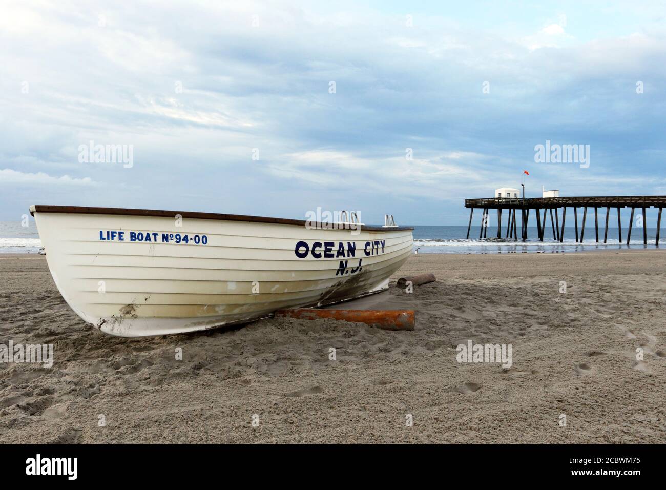 Ein Ocean City New Jersey Life Boot am Strand mit dem ikonischen Ocean City Fishing Club Pier dahinter. Ocean City, New Jersey, USA Stockfoto