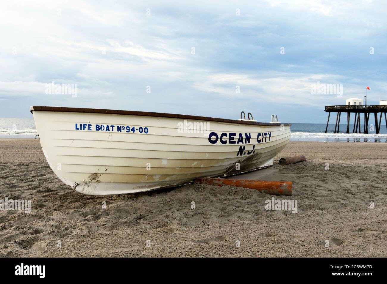 Ein Ocean City New Jersey Life Boot am Strand mit dem ikonischen Ocean City Fishing Club Pier dahinter. Ocean City, New Jersey, USA Stockfoto