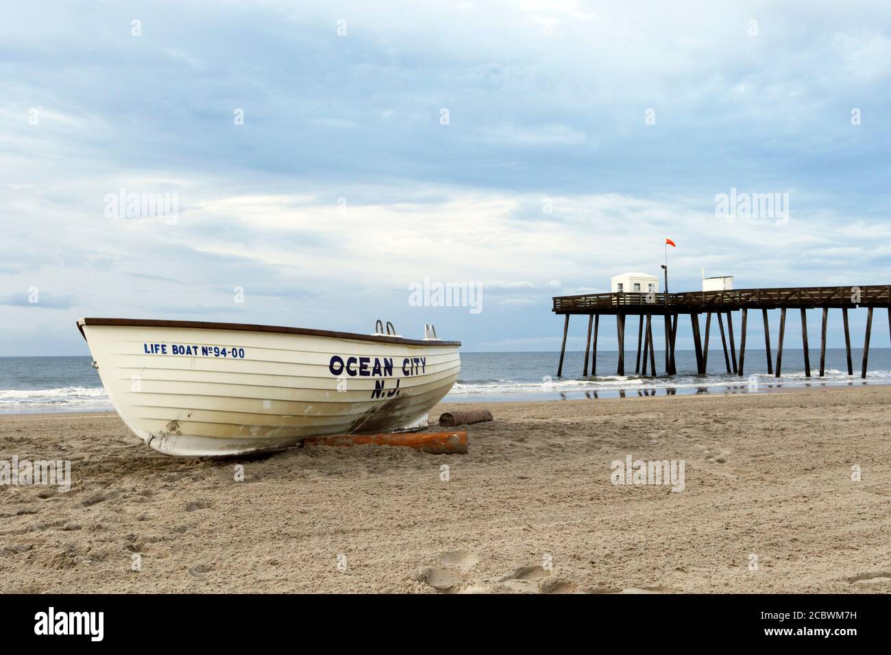 Ein Ocean City New Jersey Life Boot am Strand mit dem ikonischen Ocean City Fishing Club Pier dahinter. Ocean City, New Jersey, USA Stockfoto