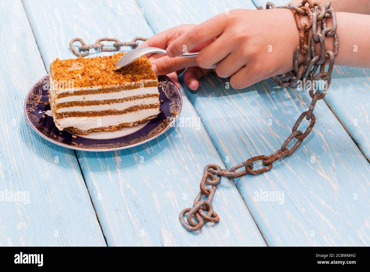 Mädchen essen leckeren Kuchen auf hellblauem Hintergrund. Hände mit Ketten gebunden. Stockfoto