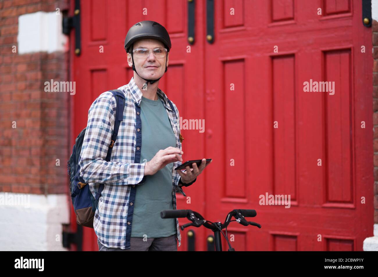 Reifer Kaukasischer Mann in einem Fahrradhelm mit seinem Fahrrad Und Smartphone in einer Stadt Stockfoto