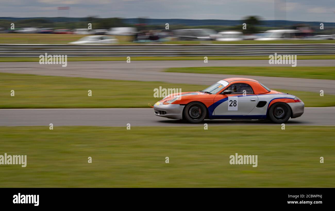Eine Schwenkaufnahme eines silbernen und orangenen Rennwagens, der eine Rennstrecke fährt. Stockfoto