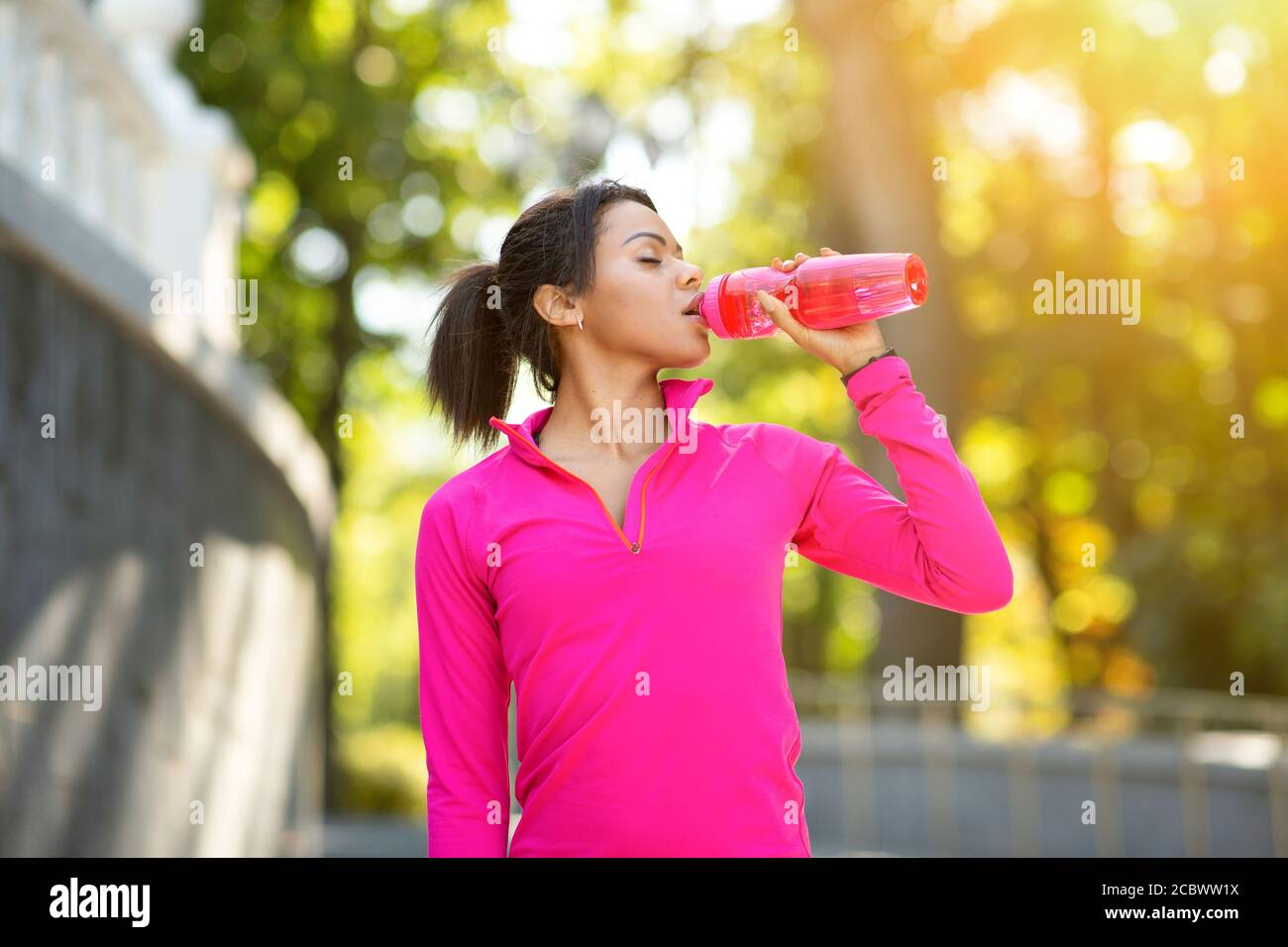 Schwarzes Mädchen in rosa Sweatshirt Trinkwasser beim Joggen Stockfoto