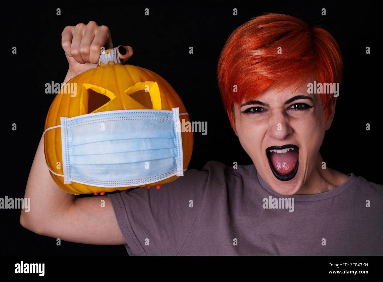 Schreiendes Mädchen mit Kürbis mit Gesichtsmaske - halloween in Das Alter des Coronavirus Stockfoto
