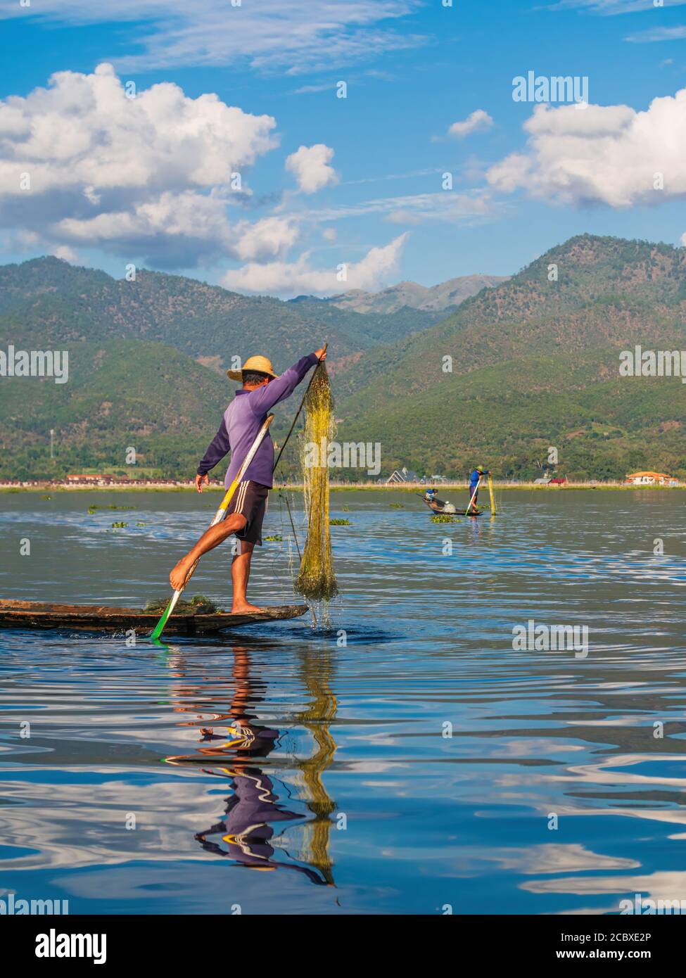 Inle Lake, Myanmar - 4. Januar 2018: Junger Burmesischer Fischer paddeln ein Boot mit einem Bein, während er sein Fischernetz benutzt Stockfoto