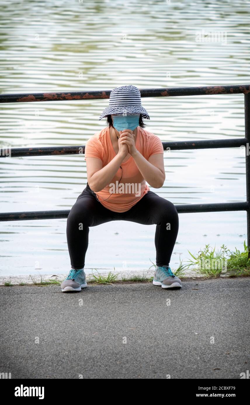 Eine flinke asiatische amerikanische Frau trägt eine Maske erstreckt sich vor dem Training. In Kissena Park, Flushing, New York City. Stockfoto