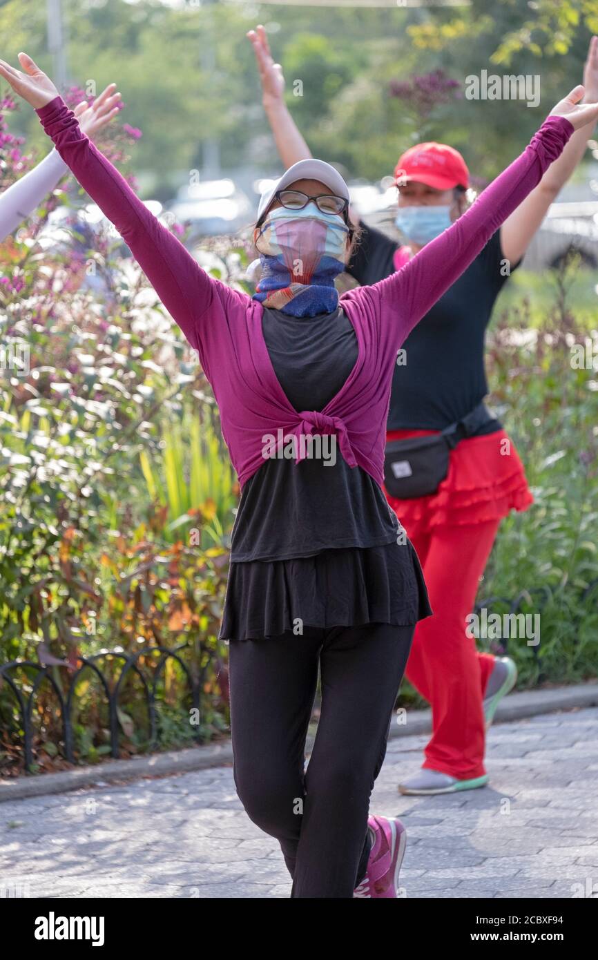 Ein chinesisch-amerikanischer Tanzunterricht Instruktor trägt eine chirurgische Maske & ein kunstvoll verzierten Gesichtstuch . In einer Klasse in einem Park in Flushing, Queens, New York City. Stockfoto