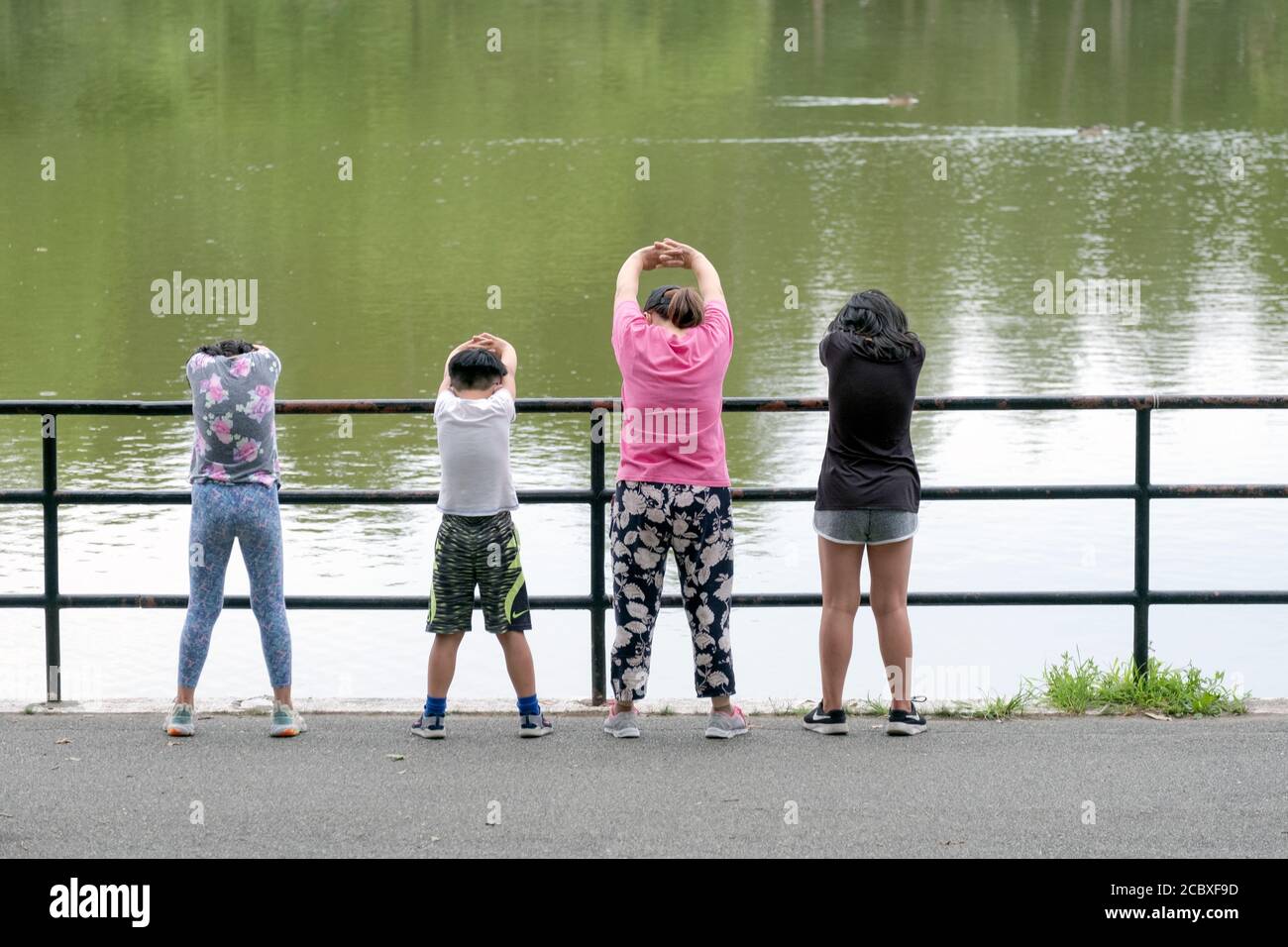 Eine asiatisch-amerikanische Mutter und ihre Kinder strecken sich gemeinsam am See im Kissena Park vor einem frühen Morgenspaziergang. In Flushing, Queens, N. Stockfoto