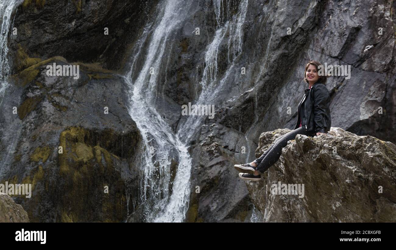Das Mädchen sitzt auf einem Felsen neben einem Wasserfall. Powerscourt Waterfall, Wicklow Mountains, Irland. Stockfoto