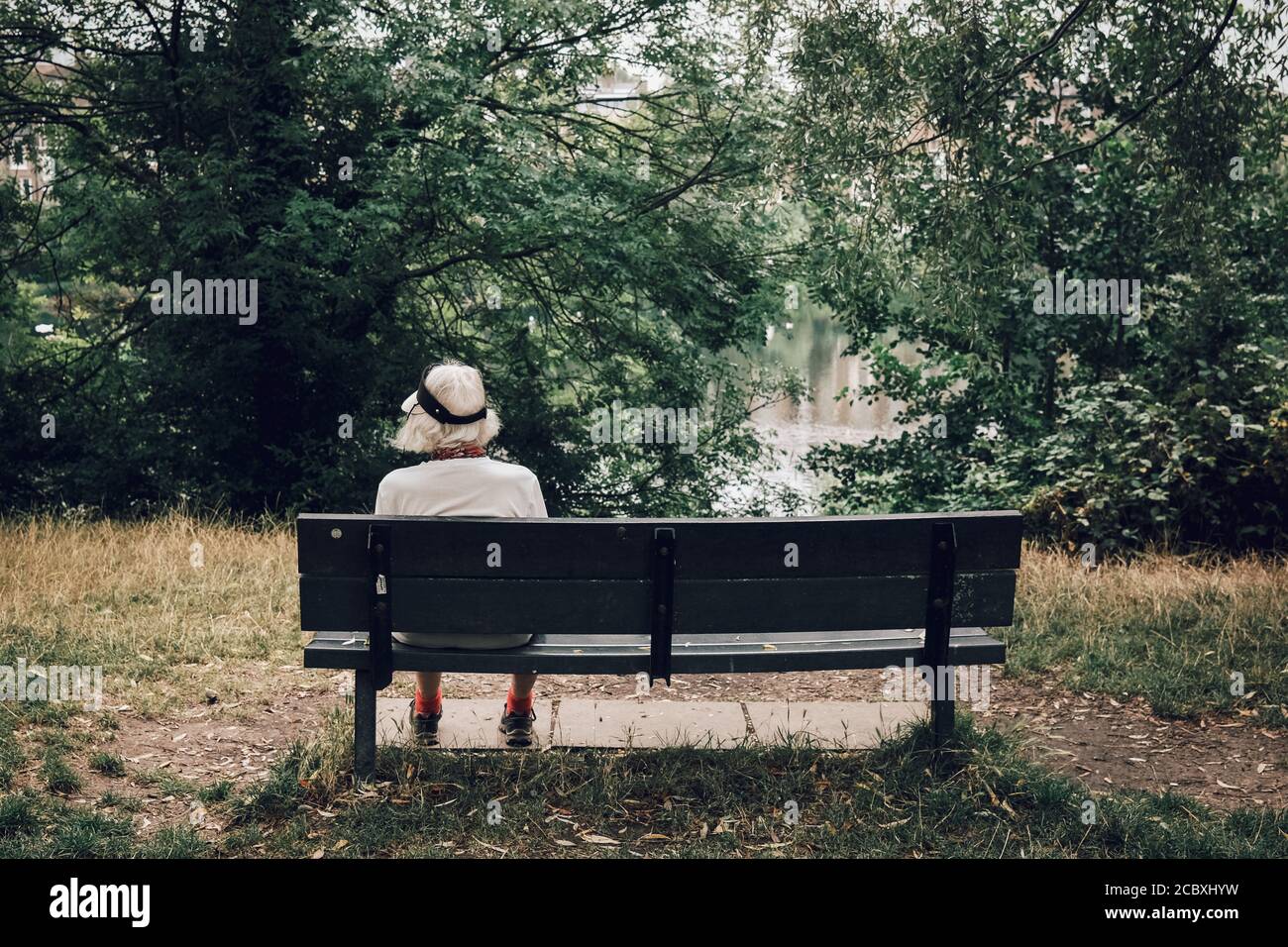 Farbbild einer älteren Frau, die allein auf einer Bank in Hampstead Heath, London sitzt. Stockfoto