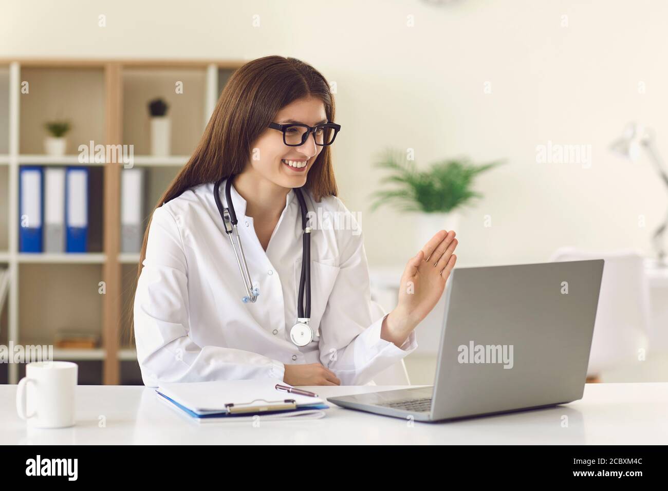 Frau Arzt Gruß Patienten Videocall online auf Laptop in der Klinik Stockfoto