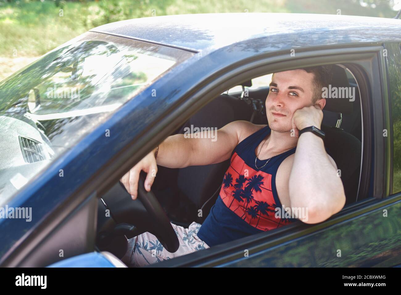 Porträt von lächelnden jungen Mann in einem Auto sitzen und Blick auf die Kamera an einem sonnigen Tag Stockfoto