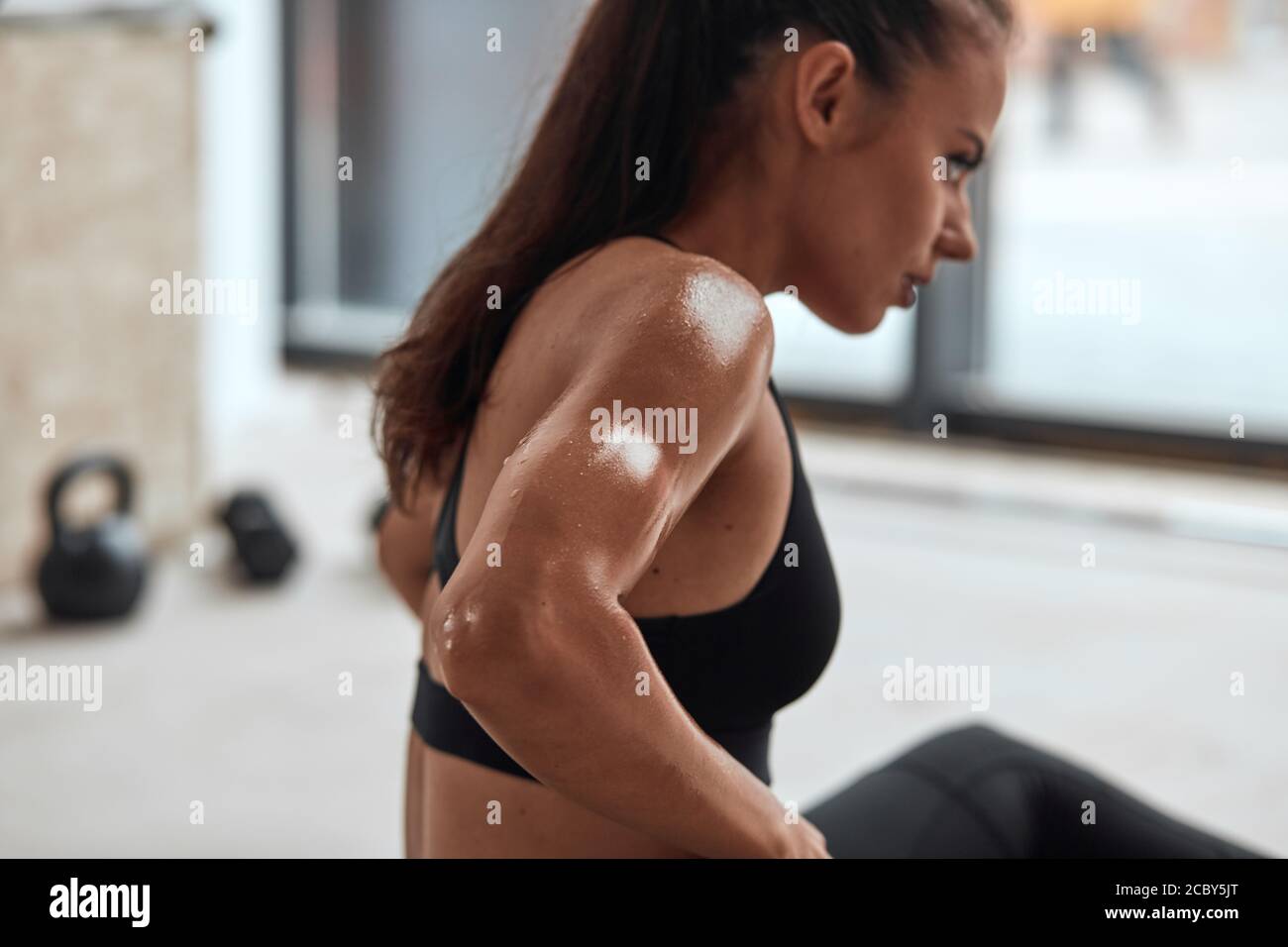 Schwitzen erschöpfte Sportlerin sitzt auf dem Boden im Fitnessstudio nach Fitness-Übungen. Konzept für Erholung und Wohlbefinden. Seitenansicht Stockfoto