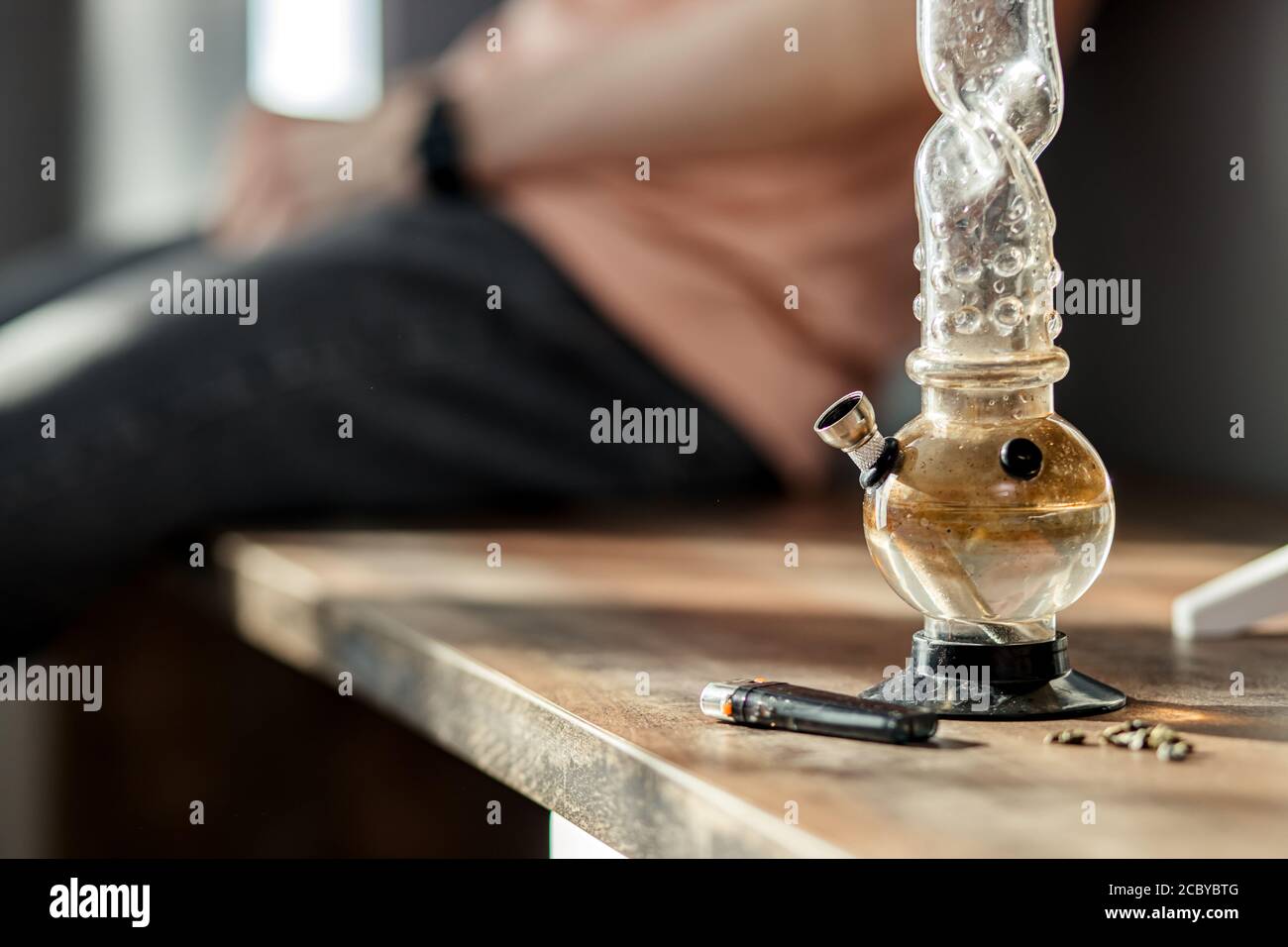 Nahaufnahme der Bong-Flasche mit Marihuana, Feuerzeug und Hanf Medizin auf dem Tisch. Drogenabhängigkeit, Ganja, Betäubungsmittel Konzept Stockfoto