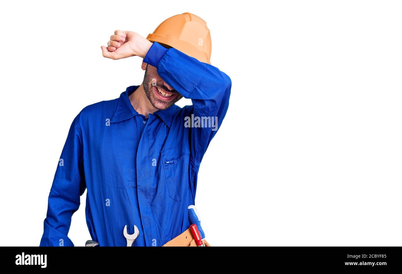 Junger hispanischer Mann trägt Arbeiteruniform, die Augen mit Arm bedeckt, lächelnd und lustig. Blindes Konzept. Stockfoto