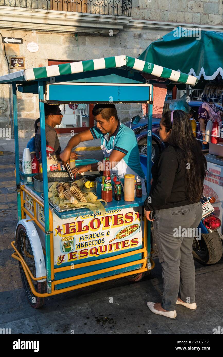 Ein Verkäufer, der Eloten und Ezitate auf der Straße im historischen Zentrum von Oaxaca, Mexiko verkauft. Elotes sind Mais auf dem Kob, die zuerst gekocht werden, dann Stockfoto