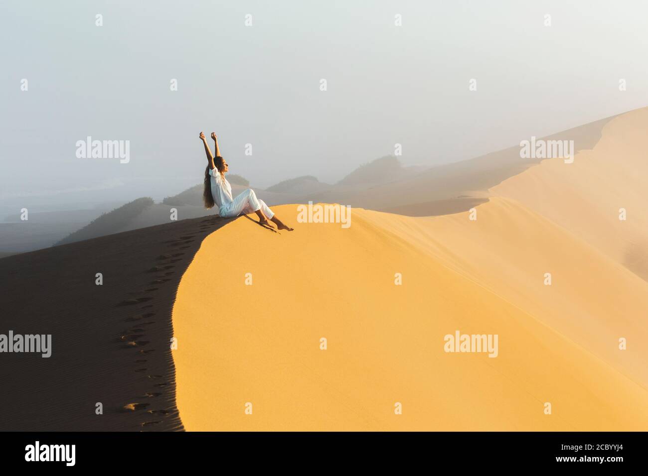 Traumziel, Reise- und Fernweh-Konzept. Glückliche Frau inspiriert von fantastischen Sonnenaufgang in Sahara Wüste Sanddünen, Marokko. Nebel am Morgen und warmes Licht. Stockfoto