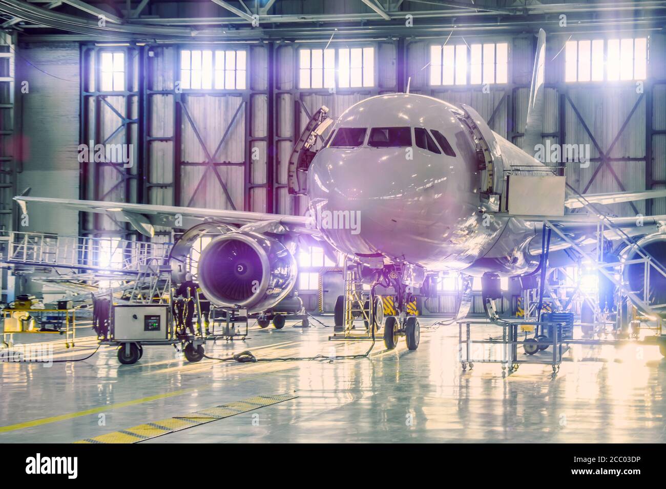 Zivile Flugzeug Jet auf die Wartung von Motor und Rumpf überprüfen Reparatur im Flughafen Hangar. Heller, violetter Farbton am Tor Stockfoto