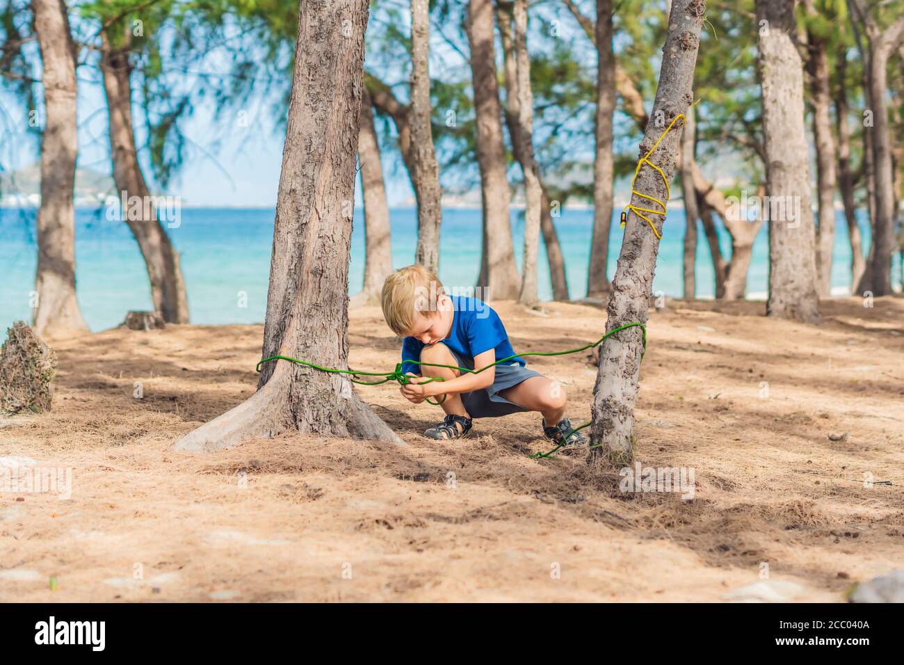 Camping Menschen Outdoor-Lifestyle-Touristen im Sommerwald in der Nähe lazur Meer. Blonde ernsthafte Junge in blauen T-Shirt Studie Überlebenstechniken, Praxis Stockfoto