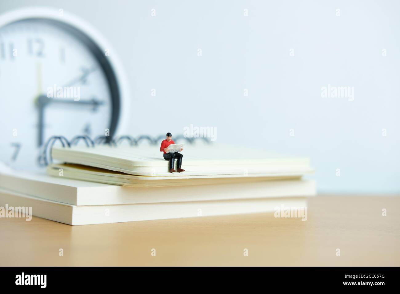 Miniatur Menschen für Morgen Lesung Zeit Konzept - junger Mann Sitzplätze über dem Bücherstapel beim Lesen einer Zeitung Stockfoto