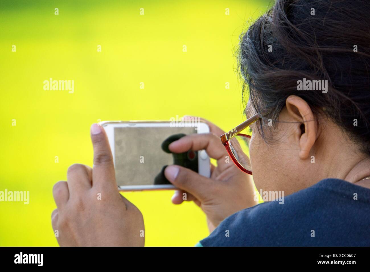 Junge Frau fotografieren mit iPhone im Freien mit einem grün gelben Hintergrund. Stockfoto