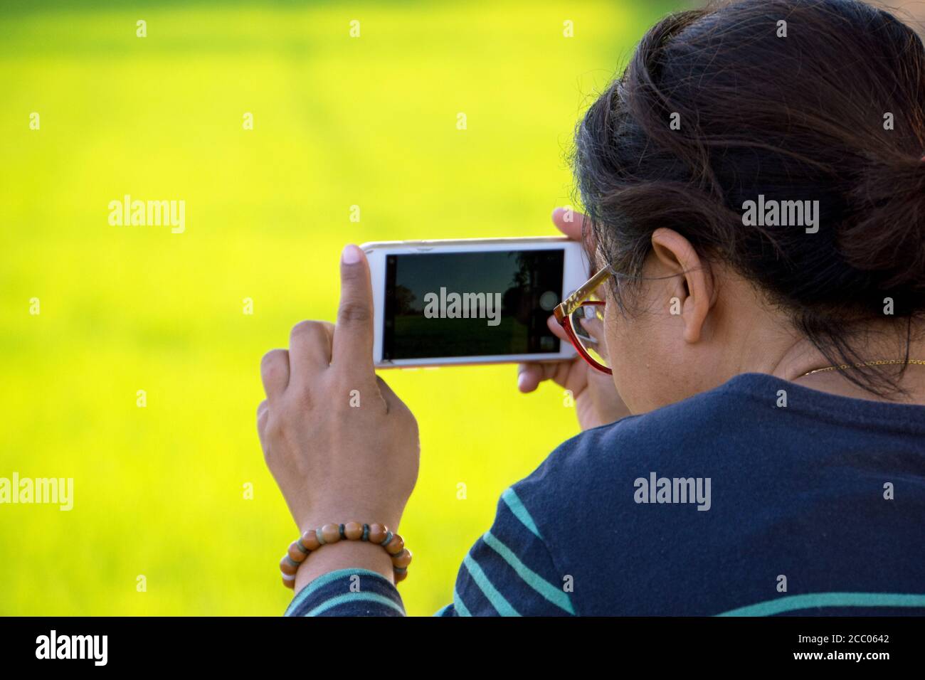 Junge Frau fotografieren mit iPhone im Freien mit einem grün gelben Hintergrund. Stockfoto