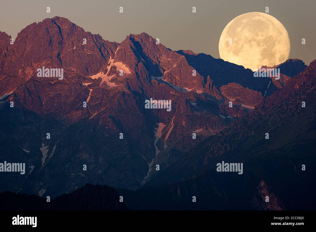 Der Vollmond geht hinter dem Gipfel des Berges unter, der von der gerade aufgehenden Sonne beleuchtet wird Stockfoto