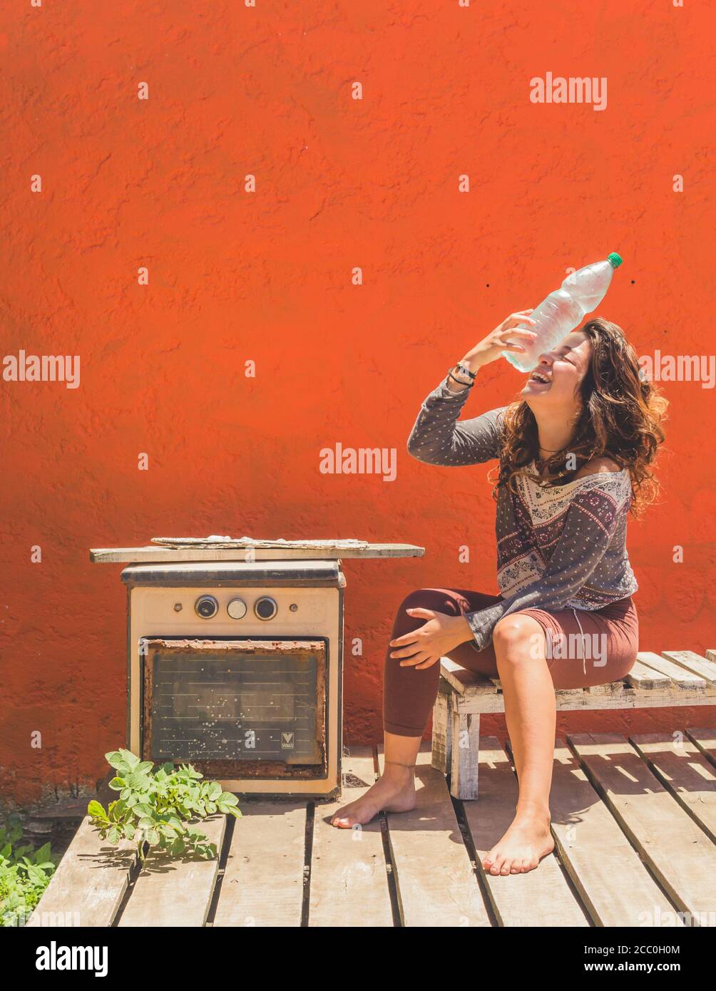 Junge Frau sitzt auf einer Holzbank und hält eine Kalte Flasche Wasser unter dem Sonnenlicht Stockfoto