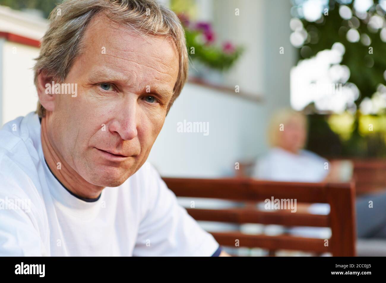 Der alte Mann sitzt im Sommer vor seinem Haus Und sieht ernst aus Stockfoto